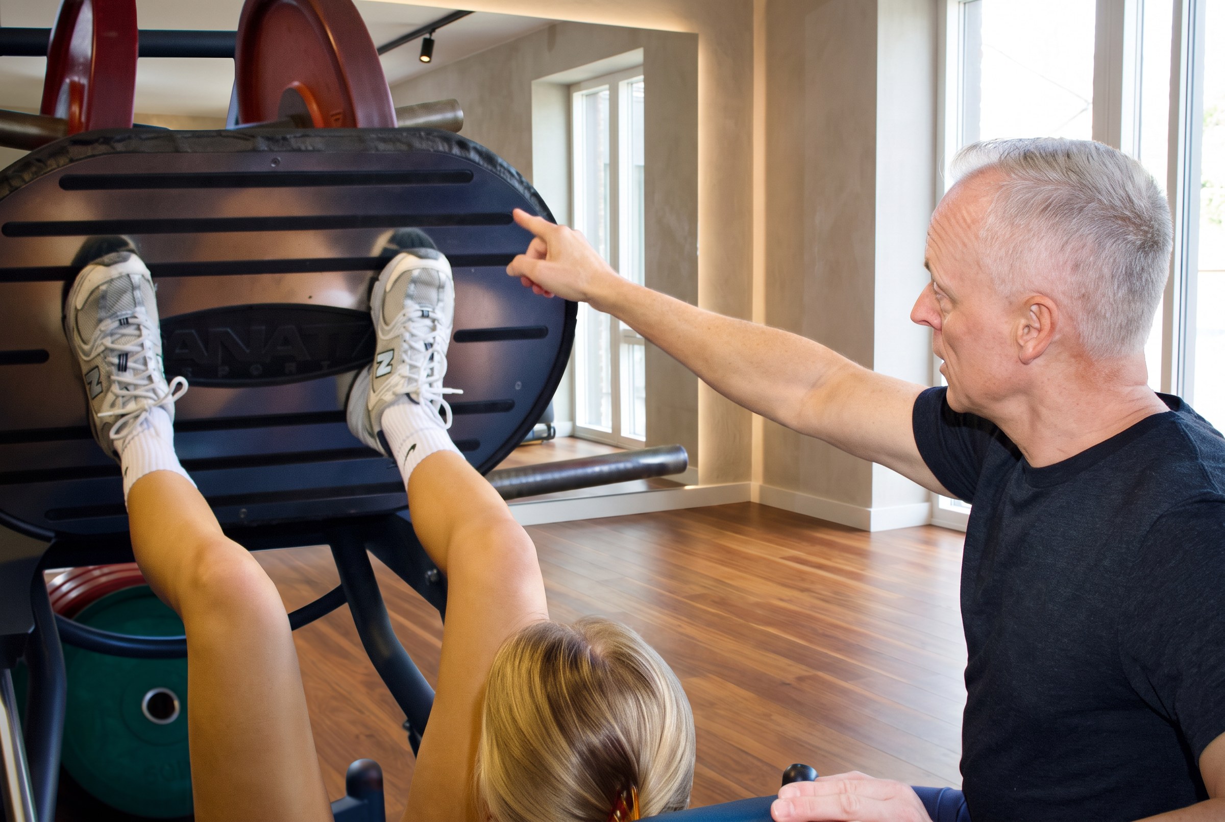 Alain begeleidt een klant aan de leg press met een coachend gebaar